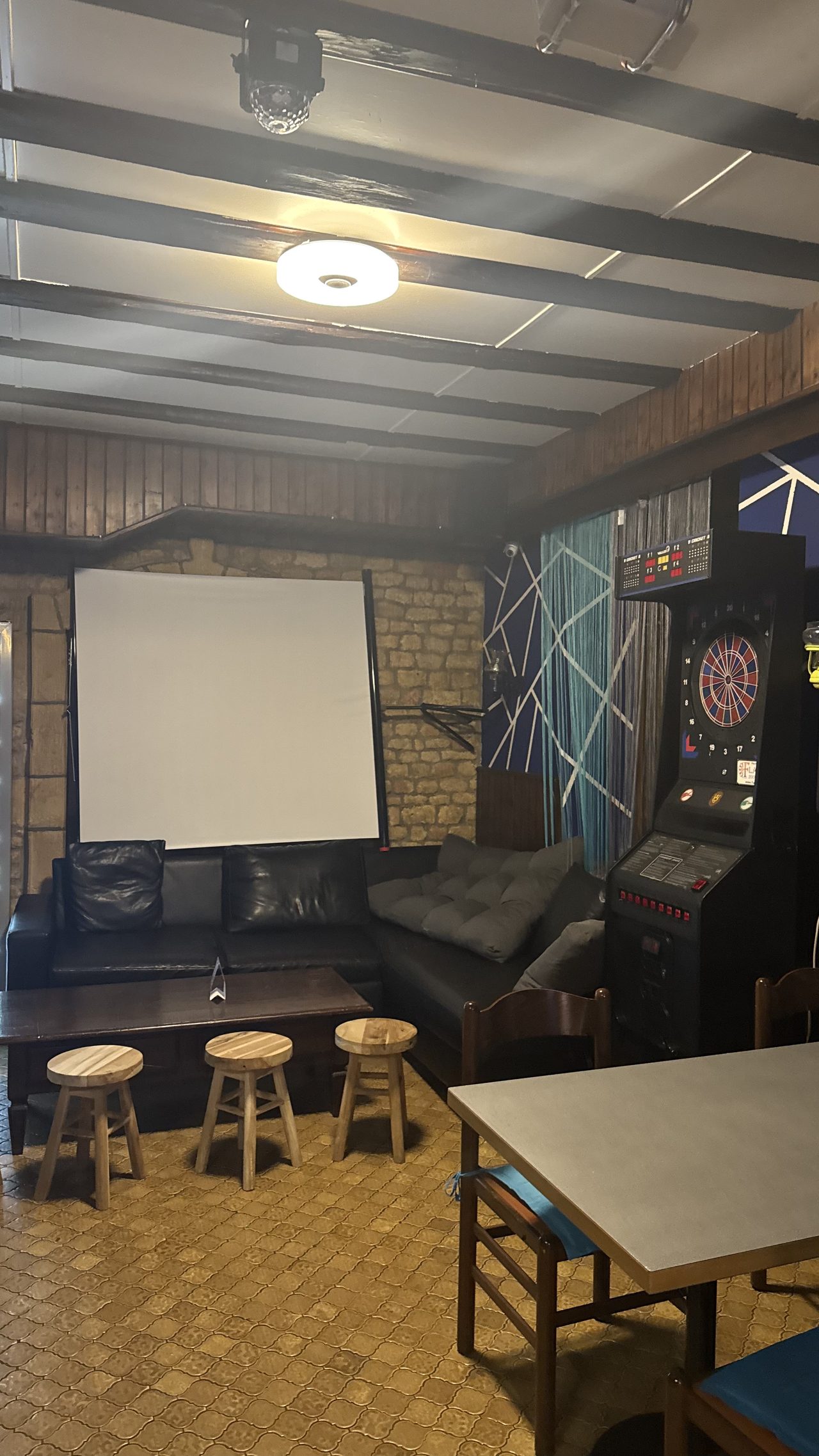 Espace lounge avec écran de projection, dartboard électronique et canapés