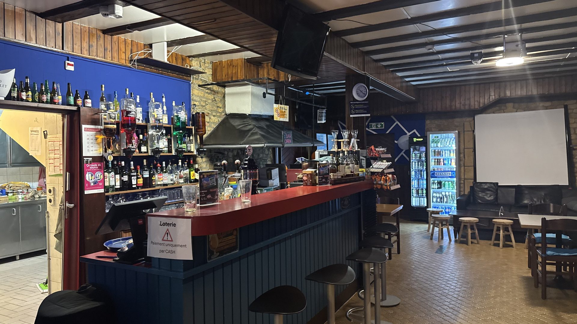 Vue large du Bar Le Forgeron avec son comptoir rouge, bouteilles et tabourets